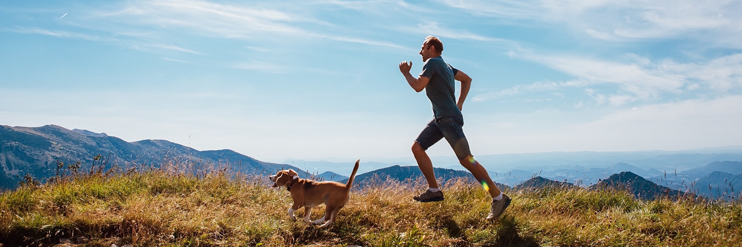 Man running with his beagle on trail across ridge